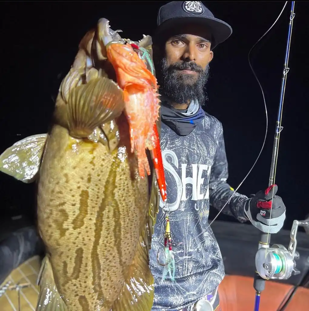 Pescador de noche sujetando un gran mero y un pargo rojo capturados pescando a fondo en Maldivas