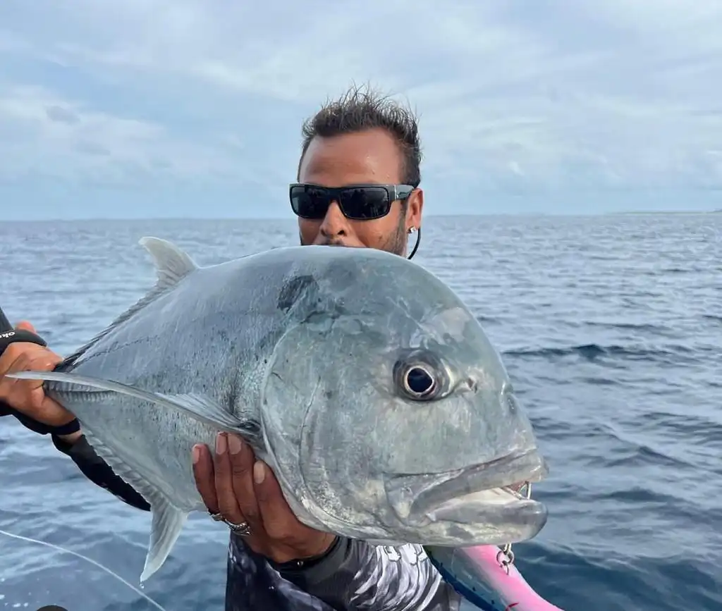 Angler in sunglasses holding a giant trevally caught popping from a boat in the Maldives