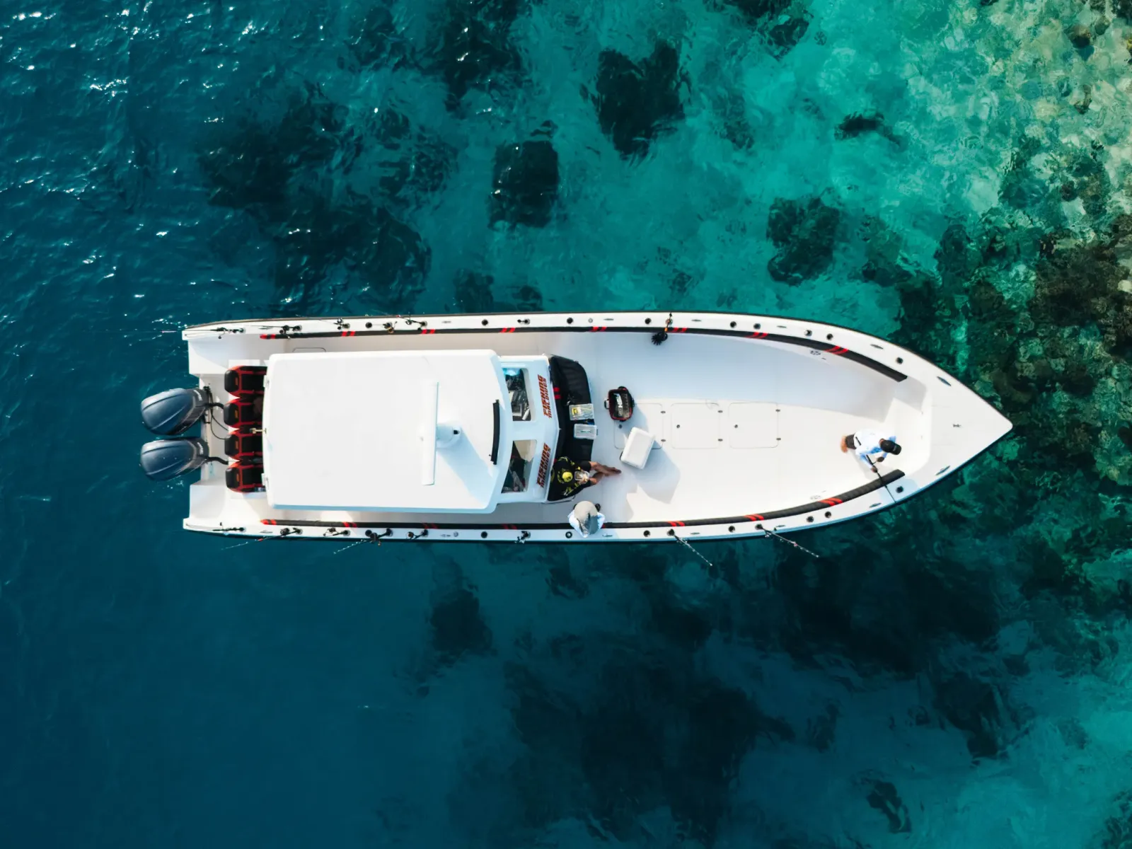 Top-down aerial view of a white fishing boat over a coral reef edge in the Maldives